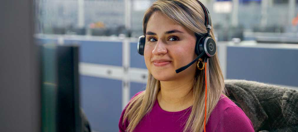 Customer service agent wearing headset viewing digital data screens with UI graphics in a modern contact center setup.